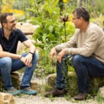 Stefan und ein Kunde, auf Steinen sitzend und lachend in einem schönen Garten