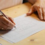 Architekturplan auf Tisch mit Händen einer Person, die darauf zeichnet